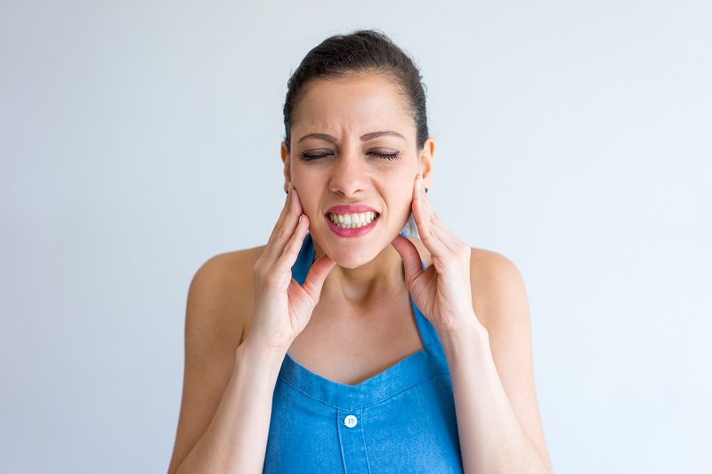 Annoyed young woman suffering from toothache and touching jaw. Irritated girl with closed eyes gritting teeth from pain. Hurt concept